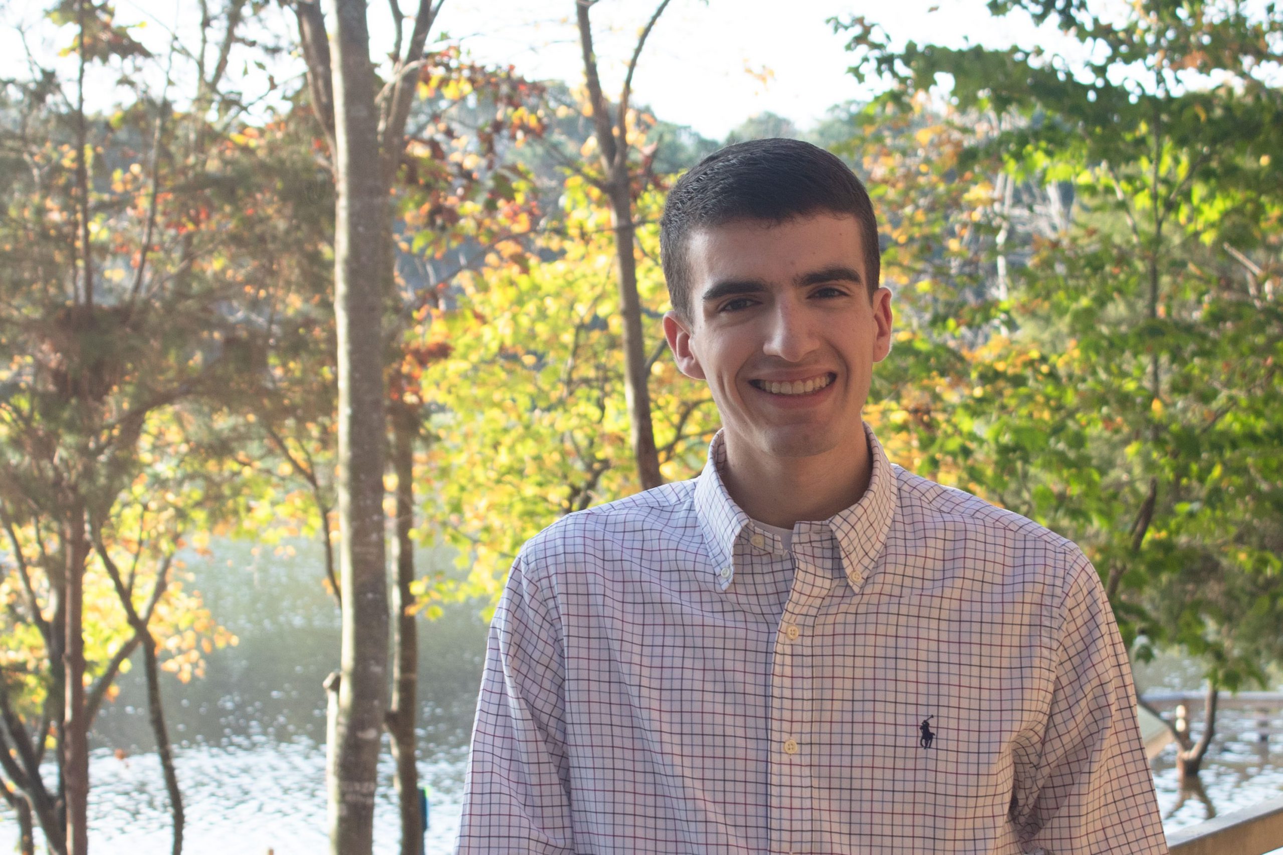 Ryan Catalfu - Photo - white male with brown hair, wearing a button down shirt with trees and water in the background.